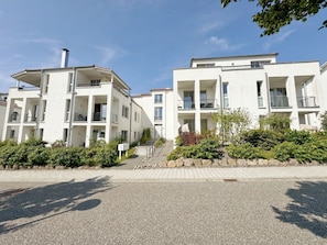 Moderni kerrostalo, jossa on useita parvekkeita ja päällystetty sisäänkäyntialue.