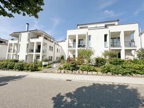 A modern apartment building with multiple balconies and a paved entrance area.
