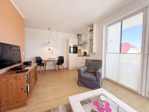 Moderni olohuone, jossa on litteänäyttöinen televisio, puuhuonekalut, harmaa nojatuoli ja suuri ikkuna, josta avautuu näkymä ulos.