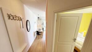 A hallway with a dining area, a white door leading to a room with a bed, and a wall-mounted mirror. - A: Villa Antje Whg. 12 with balcony - Villa Antje Whg. 12 with balcony (Göhren)