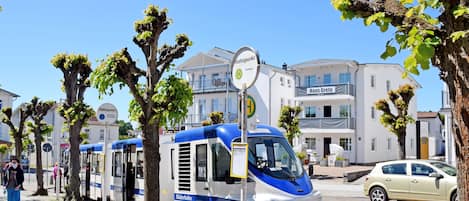 A tram station with a tram, a building labeled 'Haus Greta,' and a car parked nearby.