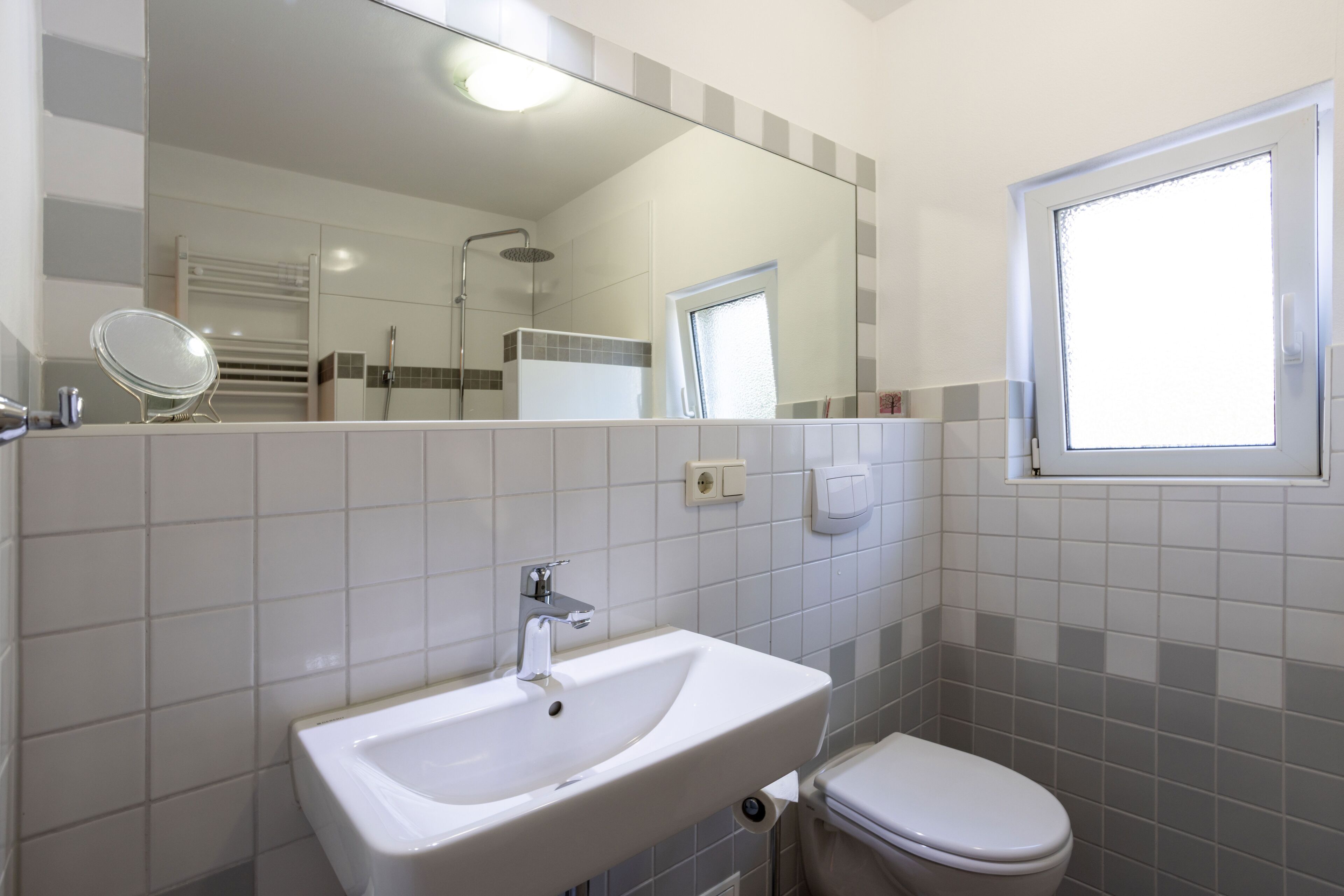 Een badkamer met een wastafel, toilet, spiegel en een raam.