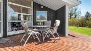 Eine Terrasse im Freien mit einem runden Tisch, vier Stühlen, großen Fenstern und Blick auf einen Garten.
