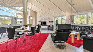 Ein geräumiger Wohnbereich mit rotem Teppich, einem schwarzen Ledersofa und einem Esstisch mit Stühlen.