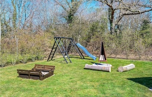 Children can play on the swing set and slide in this park area surrounded by trees and shrubs.