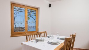 Un comedor con una mesa dispuesta para cuatro, una ventana que ofrece vistas al agua y colinas, y un equipo de aire acondicionado instalado en la pared.