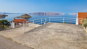 Una escalera de hormigón que lleva a una terraza con vistas a una masa de agua tranquila, una isla distante y acantilados rocosos.