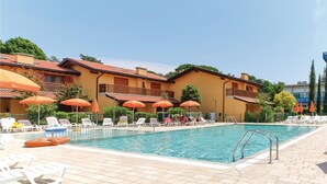 A swimming pool with lounge chairs and umbrellas, surrounded by yellow buildings with balconies.
