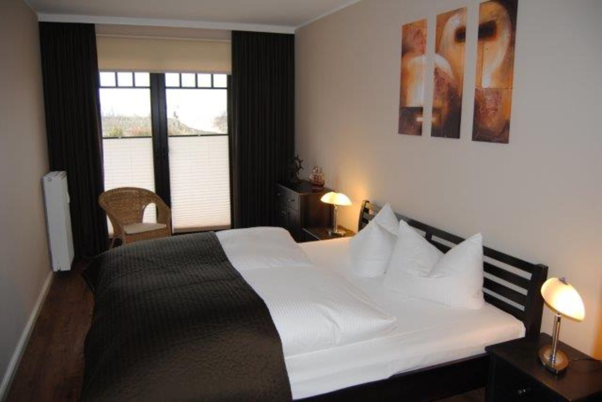 A hotel room with a large bed, a chair, a nightstand, and artwork on the wall.