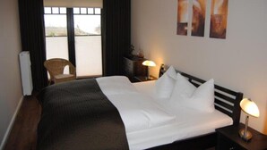 Ein Hotelzimmer mit einem großen Bett, einem Sessel, einem Nachttisch und Kunstwerken an der Wand.