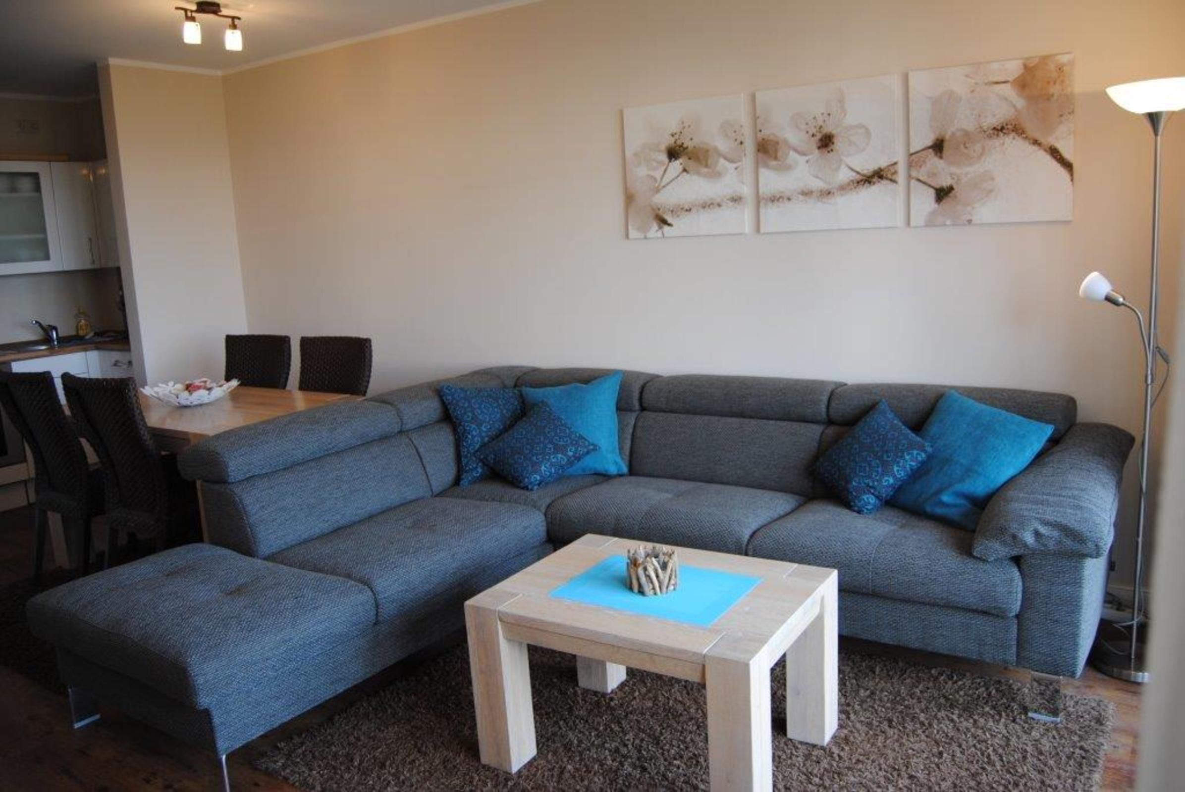 A modern living room with a grey sectional sofa, a small wooden coffee table, and a dining area with a table and chairs.