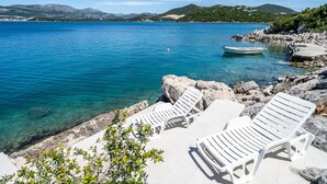 A coastal area with clear blue water, rocky shore, and white lounge chairs. - Awesome home in Janjina with sauna (Janjina)