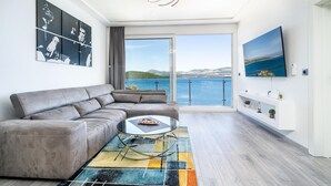 A modern living room with a grey sofa, a glass coffee table, and a colorful rug. There are abstract wall art pieces and a TV mounted on the wall. - Awesome home in Janjina with sauna (Janjina)