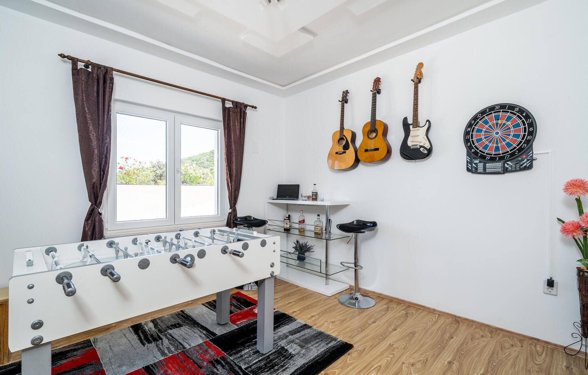Une pièce avec une table de baby-foot, des guitares, un jeu de fléchettes et une fenêtre avec des rideaux.