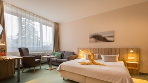 Een hotelkamer met een bed, een bureau, een stoel, een bank en een groot raam met gordijnen.