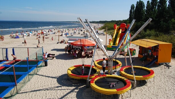Een strand met trampolines, een volleybalnet en een glijbaan.