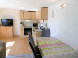 A compact kitchen with a microwave, oven, and sink. There is a television on a cabinet, and a chair is visible.
