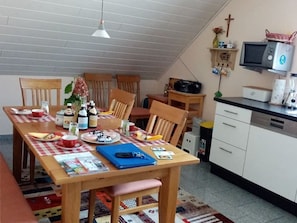En matplats med ett träbord och stolar, samt ett köksområde med mikrovågsugn och skåp.