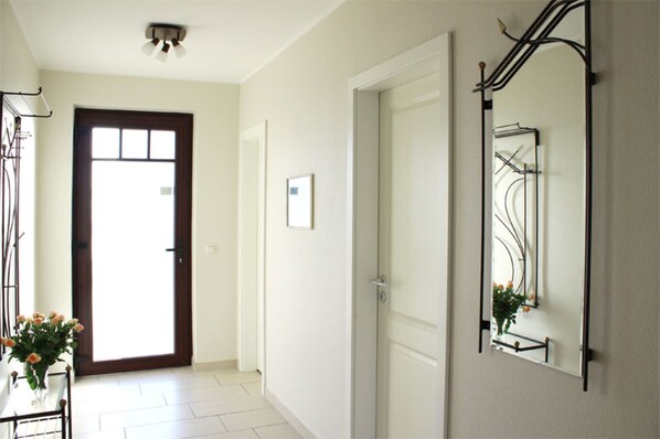 A hallway with a door, a mirror, and a small table with flowers.