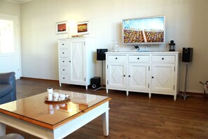 Ein Wohnzimmer mit Couchtisch aus Holz, weißen Schränken, einem Fernseher und einem Lautsprecher.