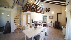 Un'ampia zona giorno con soffitto alto, una scala in legno, un tavolo da pranzo con sedie, un divano e un caminetto.