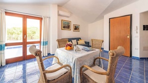 A room with a dining table set for four, wicker chairs, a sofa, and a wooden door. - Holiday apartment mit Meerblick (Cala Gonone)