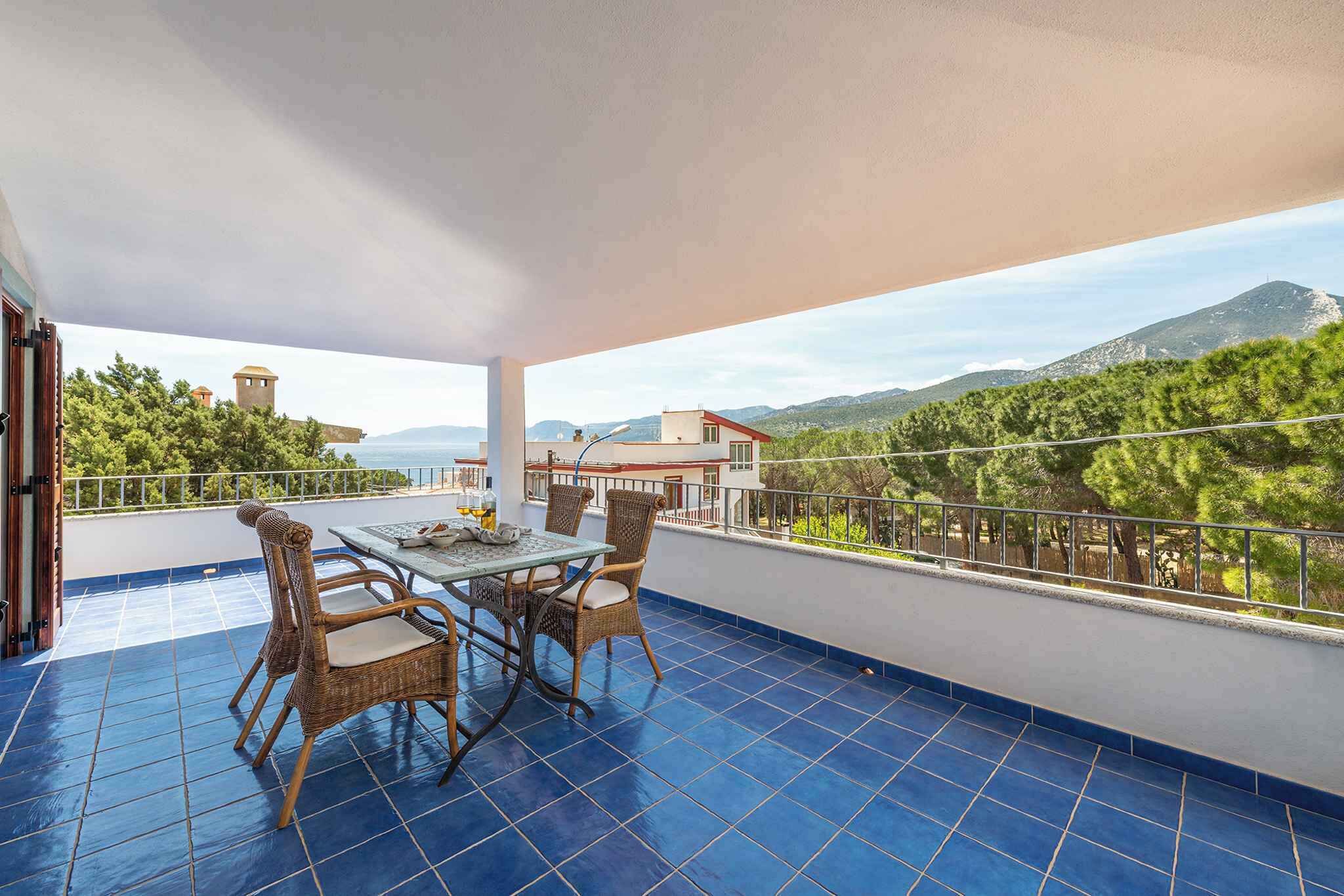 A balcony with a table and chairs, a view of a mountain and trees, and a building with a tower in the background.