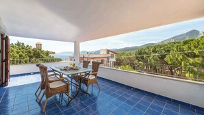 A balcony with a table and chairs, a view of a mountain and trees, and a building with a tower in the background. - Holiday apartment mit Meerblick (Cala Gonone)