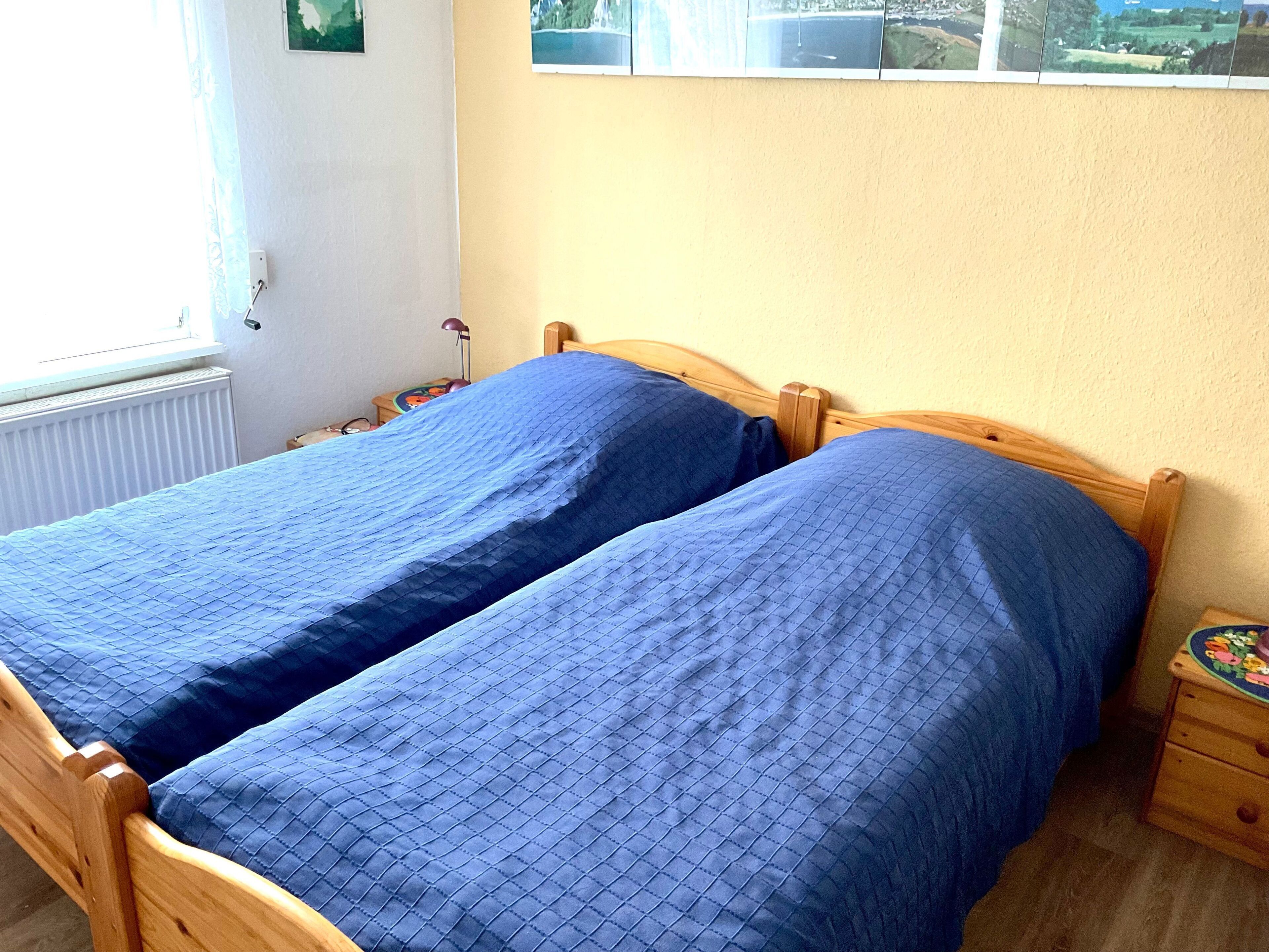 Une chambre avec deux lits simples, une tête de lit en bois, une table de chevet avec une lampe et une fenêtre donnant sur la mer.