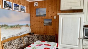 A cozy room with a wooden wall, a bench, a table with a floral tablecloth, and a white cabinet with a microwave. - Rügen-apartment 65 - apartment (Garz/Rügen)