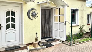 A house with a white door, a decorative moon and sun wall art, a small garden with plants and flowers, and a window with a metal grid. - Rügen-apartment 65 - apartment (Garz/Rügen)