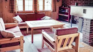 Una habitació acollidora amb taula i bancs de fusta, una llar de foc de rajola i finestres grans amb cortines.