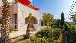 Un bâtiment à la façade en pierre, un parasol rouge et un jardin avec différentes espèces de plantes.