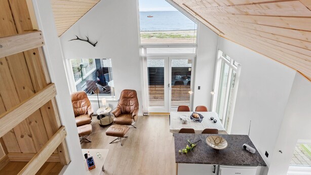 A modern interior with a dining area, seating, and a view of the sea.