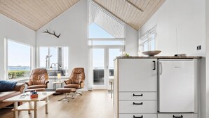 A spacious living room with a large window, a white refrigerator, and a leather chair.