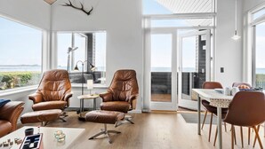 A spacious living area with leather chairs, a coffee table, and a view of the sea through large windows.
