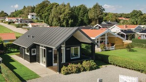 A small, modern house with a dark roof and white trim, number 110, surrounded by well-maintained lawns and a few trees.
