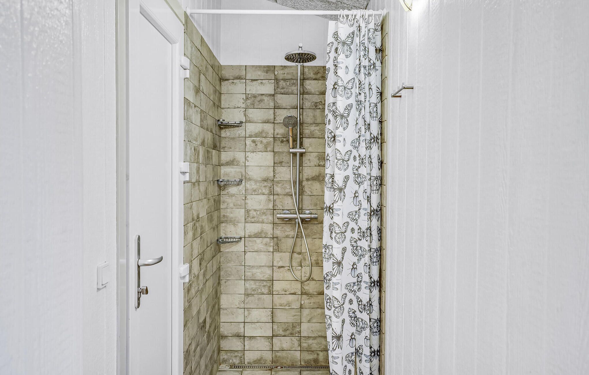 Un baño con ducha, paredes de azulejos y cortina de baño con estampado de mariposas.