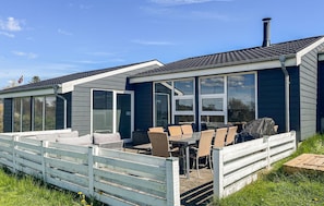 A modern house with a patio area featuring outdoor furniture and a white fence.