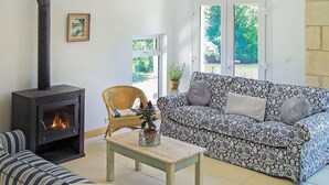 A cozy living room with a fireplace, a patterned sofa, a wicker chair, and a small table with a vase. - Beautiful home in La Barde (La Barde)