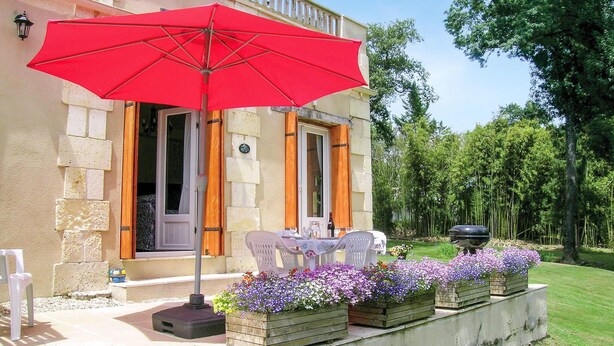 A building with a red umbrella, outdoor seating, and flower planters. - Beautiful home in La Barde (La Barde)