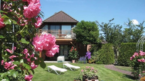 A house with a balcony, a lawn, and a garden with flowers and plants.