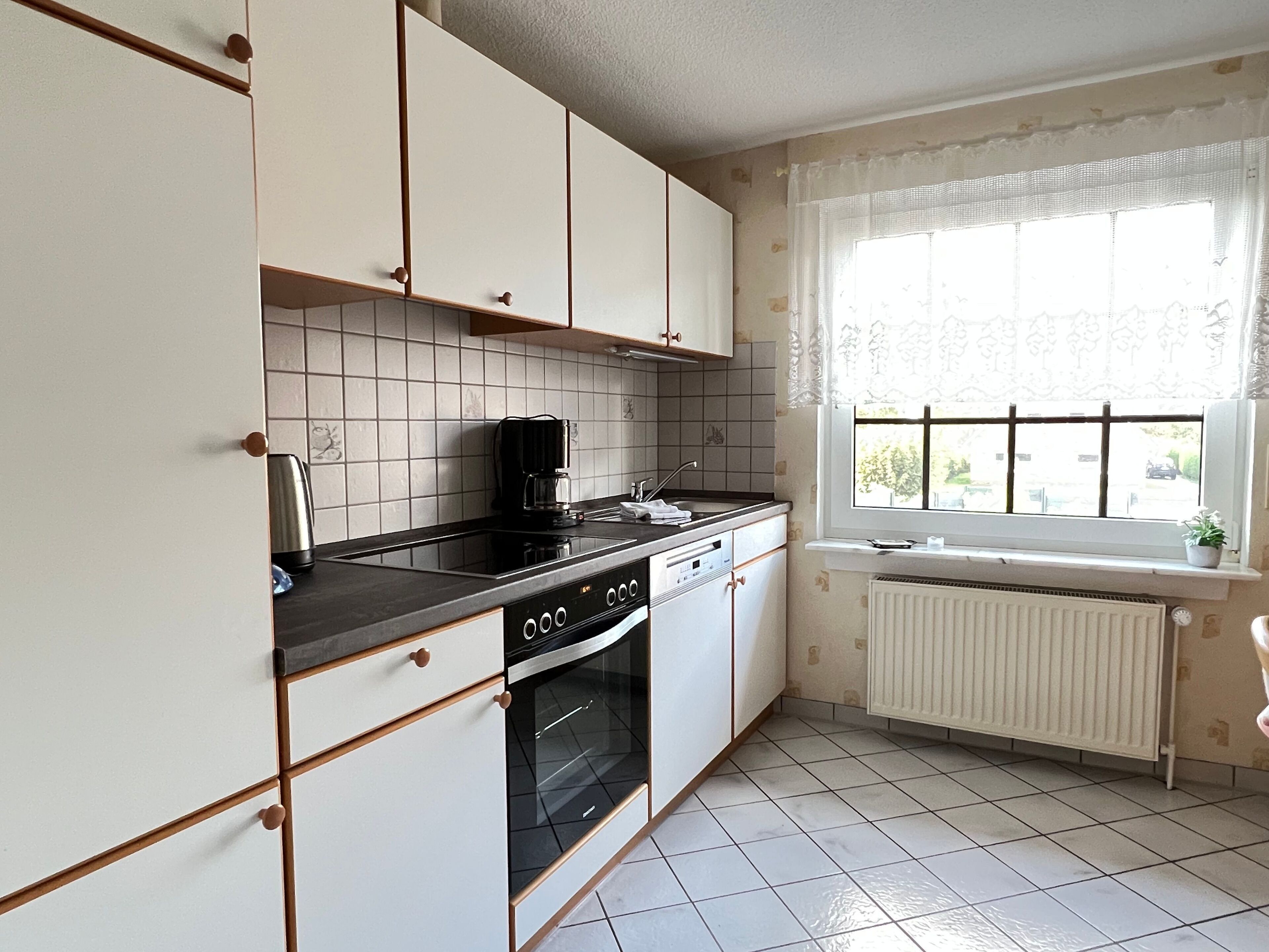 A kitchen with white cabinets, a black stove, and a window with a view of the outside.