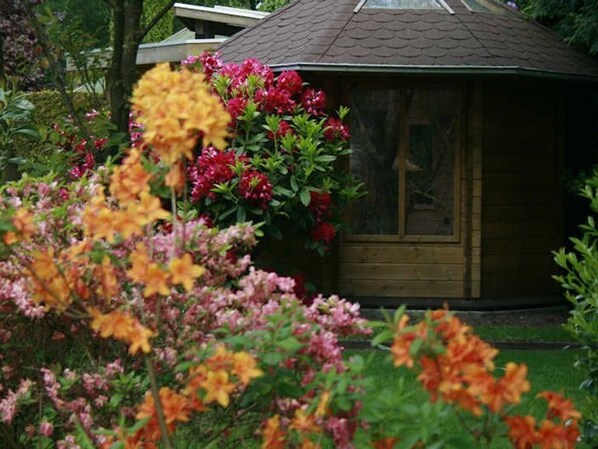 A wooden cabin with a sloped roof surrounded by vibrant flowers.