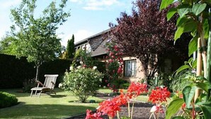 A garden with a lawn, a chair, and a house with a window.