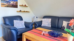 A living room with two blue leather sofas, a wooden coffee table, and a painting of a lighthouse.