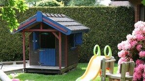 A children's play area with a slide, a small wooden playhouse, and a spring-mounted swing set.