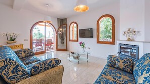 Ein geräumiges Wohnzimmer mit gemusterten Sofas, einem Glastisch und einem Kamin.