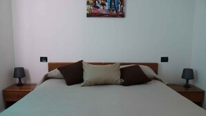 A neatly made bed with a wooden headboard, two bedside lamps, and a wall-mounted picture. - Holiday apartment with balcony (Lazise)
