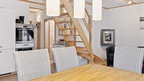 A modern kitchen with a wooden staircase, white wicker chairs, and a wooden dining table. - Ferienhaus 2 Altefähr (Altefähr/Rügen)